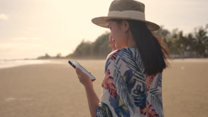 日落时分，亚洲女子在海滩上玩智能手机。