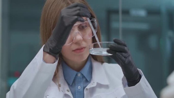 化学学院的学生在课堂上做实际工作，戴着防护眼镜和白色长袍的年轻女子肖像