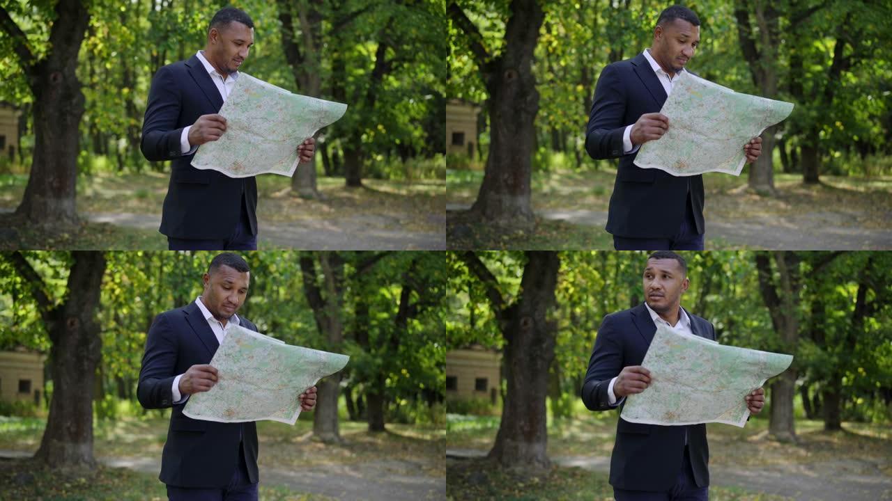 不确定英俊的年轻人站在阳光明媚的夏日公园检查纸质地图。迷失的非洲裔美国游客选择户外路线的肖像。旅游和