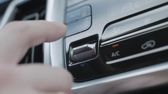 用手调节车内的空调控制按钮。气候控制按钮是银色的。自动模式下的气候系统。男子调节车内的气候控制