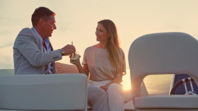 SLO MO夫妇在日落时坐在游艇的桥上，用饮料敬酒