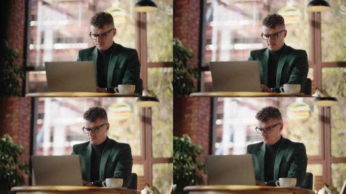 一个穿着夹克和眼镜的东方英俊男子正坐在咖啡馆里，在笔记本电脑上打字。自由职业者，远程工作。