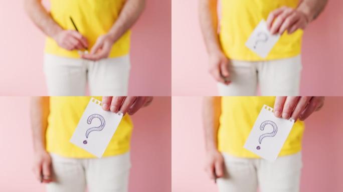一个穿着白色牛仔裤的男人在一张纸上写字，并在上面画了一个问号。粉色背景。男性疾病和阳痿的概念