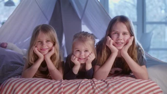 三个sistrers躺在舒适的天篷床上。看着相机微笑