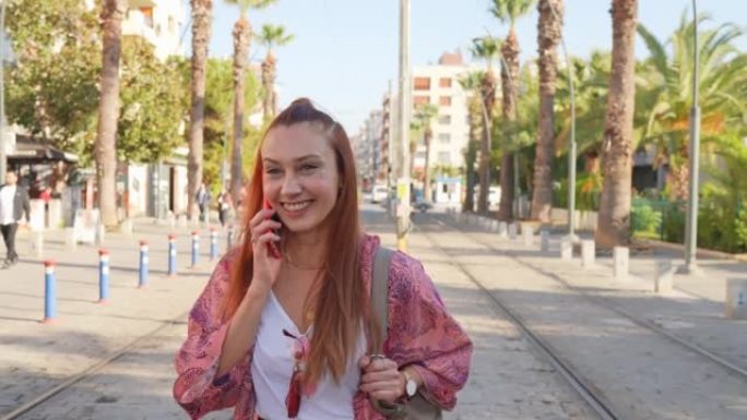 快乐的年轻女子在城市街道上行走时使用手机