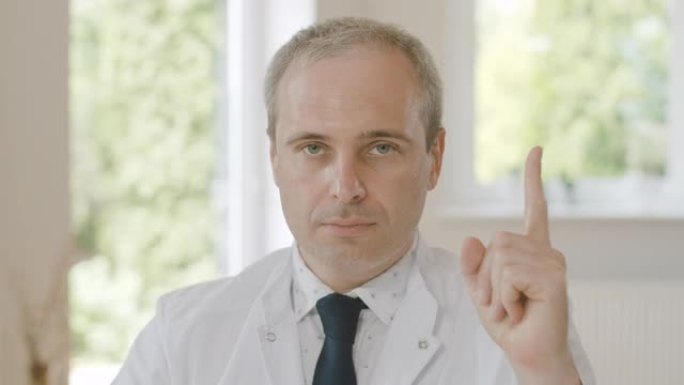 自信认真的医生坐在抬起手指看着相机的特写肖像。专业高加索中年医生在医院摆姿势。电影院4k ProRe