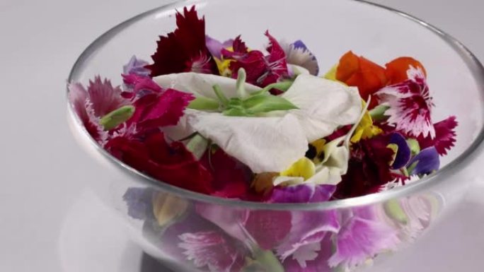 美丽的彩色黄紫罗兰wite红色食用花洒滴在贪婪的花园沙拉番茄大理石桌面碗木勺白色背景