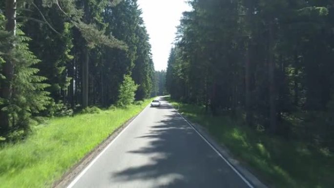 空中无人机在森林茂密的道路上射击，白色跑车驶过