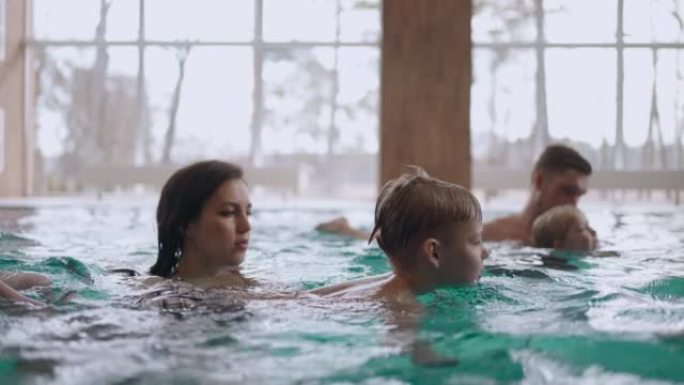 幸福的家庭在大型的健康或酒店里一起游泳，父母和孩子在温水中洗澡
