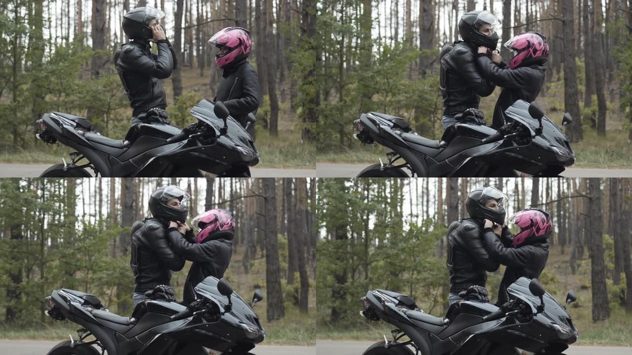自信的摩托车手戴上头盔，充满爱心的女友系紧头盔的侧视图。年轻的跨种族夫妇准备在阴天户外进行速度比赛。