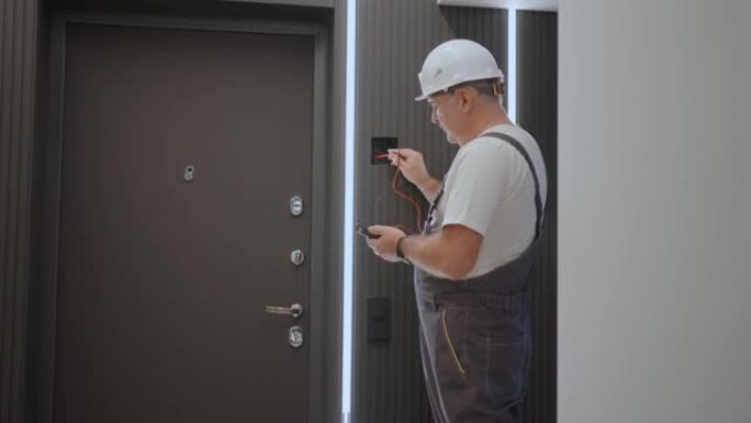 一名男电工用准备安装智能家居的电线测试仪检查网络中的电压。建筑工人修理带灯线的公寓