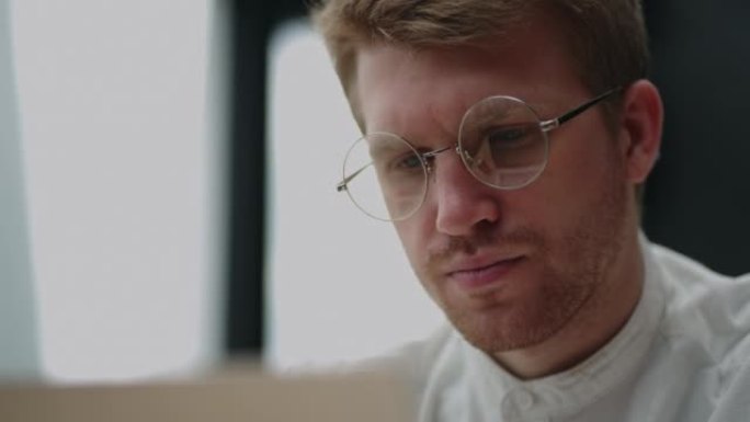 程序员或it专家正在办公室使用笔记本电脑，用眼镜拍摄帅哥的特写肖像