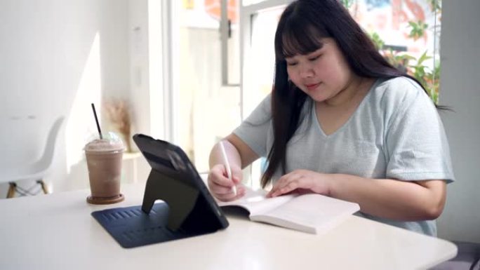 大型女性在咖啡店在线学习并在平板电脑上做笔记。