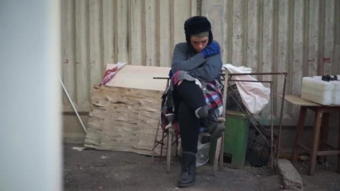 绝望的年轻无家可归的女人坐在城市的垃圾箱里，表情悲伤。高加索无房者坐在户外椅子上思考。抑郁和贫困。