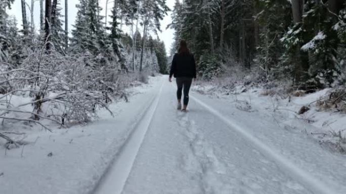 空中无人机拍摄了一名妇女在树林中沿雪道行走的镜头