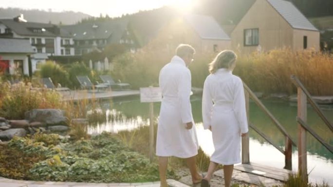 男人和女人穿着白色毛巾走向绿色池塘