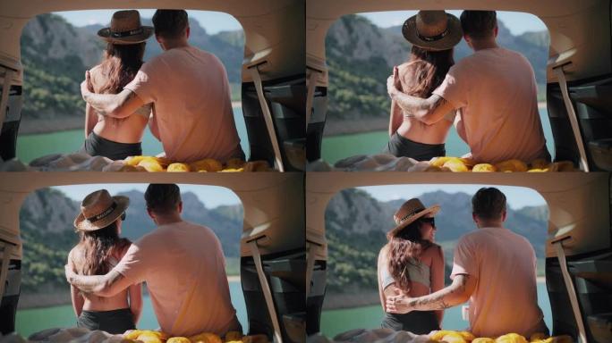可爱的年轻夫妇坐在美丽的绿松石湖边的汽车后备箱里拥抱