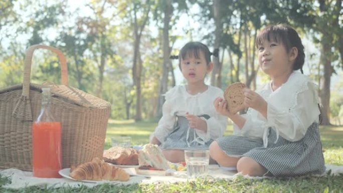 两个儿童女孩亚洲家庭享受野餐，在公园里吃绿树。