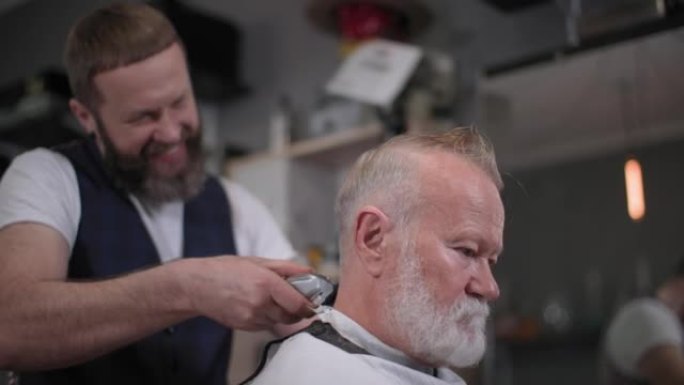 面带微笑的男理发师在理发店为一位留着胡子的老顾客修剪头发