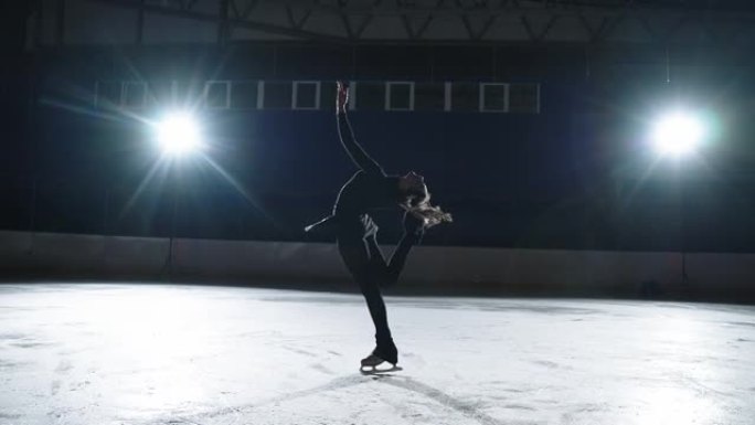 优雅的女花样滑冰运动员在黑暗中的溜冰场上进行旋转，在明亮的拱腹和轮廓下移动