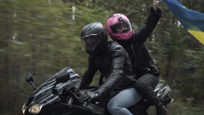 年轻的跨种族夫妇戴着头盔骑摩托车，女人举着乌克兰国旗。中东男人和高加索女人以国家象征赛车。骄傲和生活
