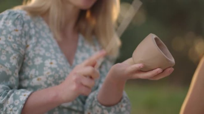 一位年轻女子在自然界的开放区域中专心地用粘土雕刻物体，享受特写镜头的过程。女孩用抹刀 (工具) 敲打