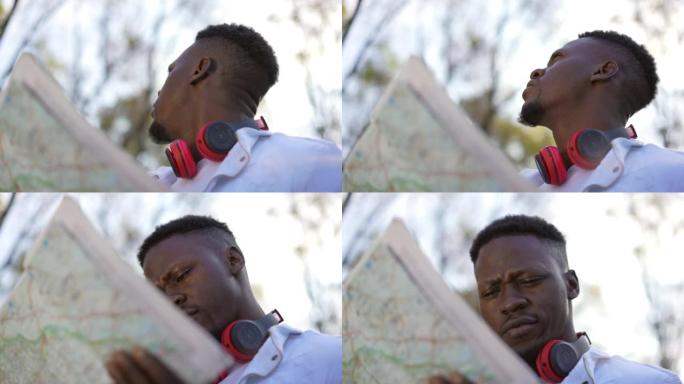 特写古玩年轻的非洲裔美国男子，纸质地图站在秋天的森林里，远望。体贴不确定的游客选择秋季户外旅行的方向
