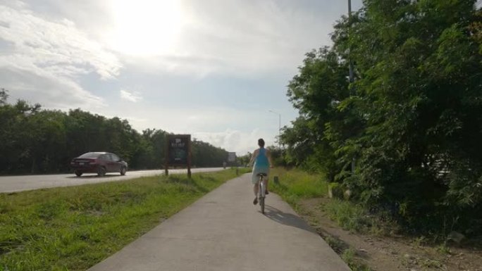 女人沿着丛林小路骑自行车，在马路旁边