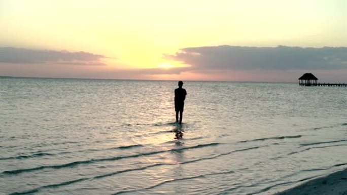 年轻人在日落时穿过低潮的海洋