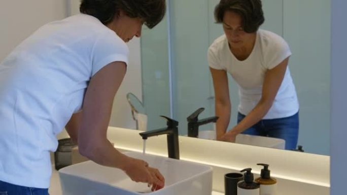 在家中的成年妇女一边照镜子一边洗手