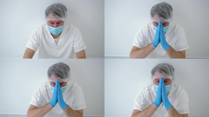 绝望的高加索医生在医院里靠在墙上祈祷的肖像。在新型冠状病毒肺炎大流行爆发的医疗诊所中，穿着制服和冠状