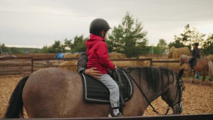 蹒跚学步的孩子第一次在小马俱乐部骑马，教练女人抱着马鞍上的婴儿，帮助他
