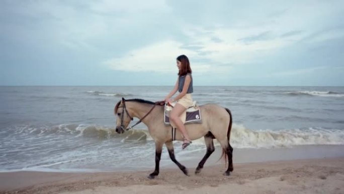 4K，一名年轻的亚洲女游客在海滩上骑马，在日落前的傍晚，游客可以骑马。海边的海滩区，波浪小，天气好。