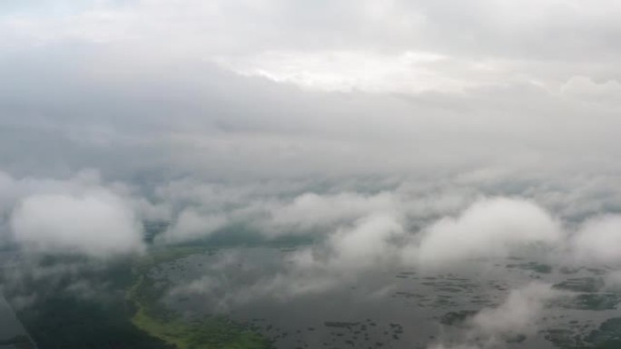 空中俯视无人机飞过蓬松的雨云，在美丽的湖边的绿色森林上滚动。从上面看松林有雾的早晨，多云，多雾的天气