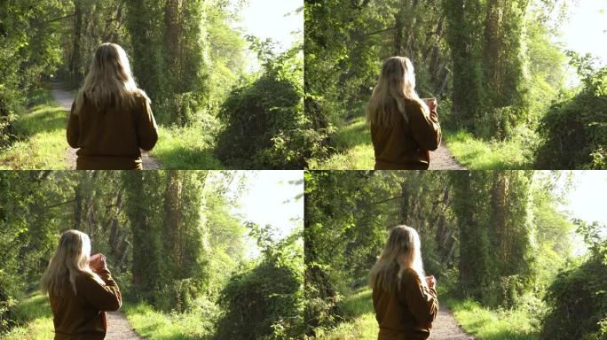 女人在森林小径上放松，拿着酒杯