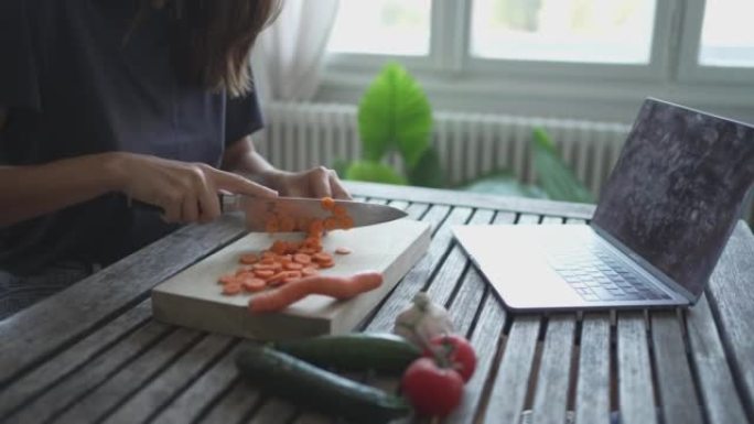 年轻女子在餐桌上切碎胡萝卜