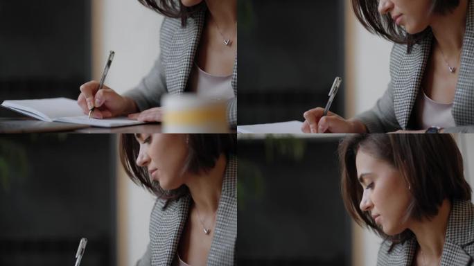 女商人在笔记本上写东西。初创女企业家学生在计算机附近的工作场所学习写作笔记。女人的手在桌子上的白色空
