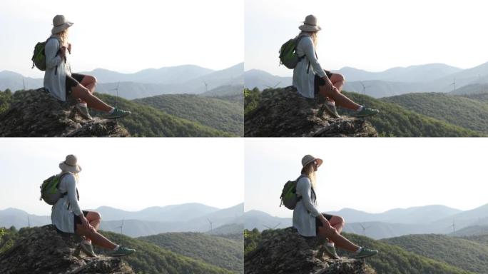 女徒步旅行者到达绿山风力涡轮机上方的岩石山顶