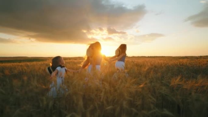 快乐的小女孩朋友或姐妹在日落时牵着手在美丽的金色麦田上奔跑