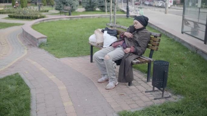 年轻的无家可归的妇女在公园的长凳上睡觉，社会问题，贫困