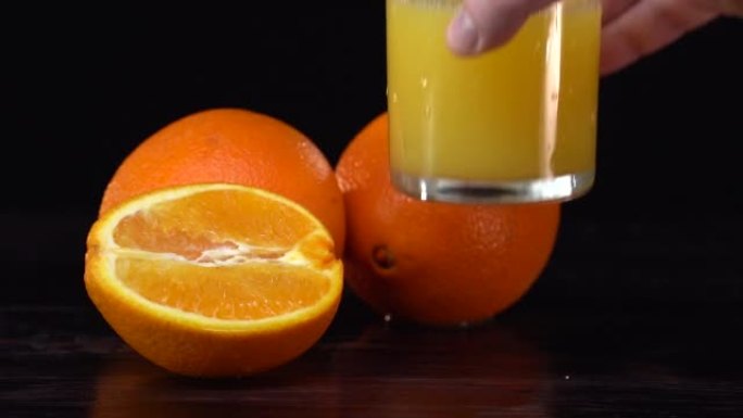 健康的橙汁在玻璃杯和橘子。白人手拿着玻璃杯，然后放在桌子上。饮食概念。黑色背景。深色反射表。慢动作