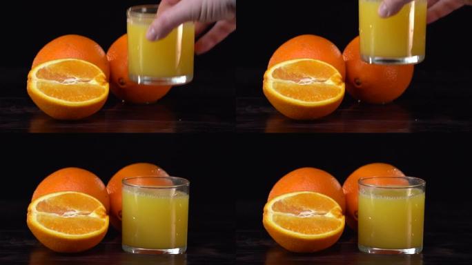健康的橙汁在玻璃杯和橘子。白人手拿着玻璃杯，然后放在桌子上。饮食概念。黑色背景。深色反射表。慢动作