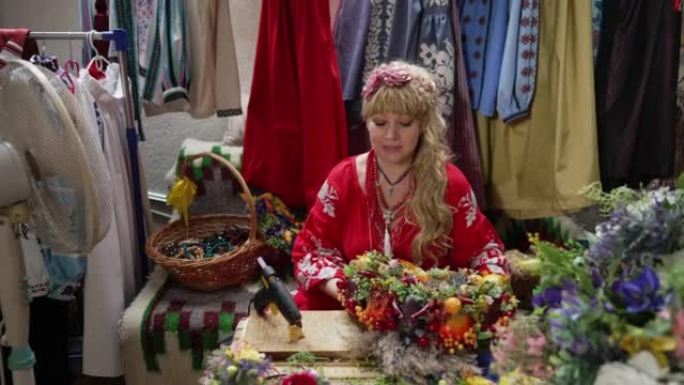 穿着传统绣花连衣裙的乌克兰美女肖像，使民族花圈以慢动作说话。积极自信的工艺人员坐在室内的桌子旁。天赋