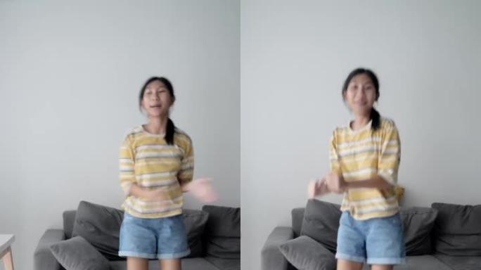 有趣的亚洲女孩在家里靠近窗户的客厅里唱卡拉ok和跳舞，生活方式的概念。