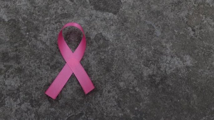 粉色丝带乳腺癌意识图标徽章放置在乡村水泥墙背景上。紫丝带世界癌症日，10月粉红日，全国癌症幸存者日概