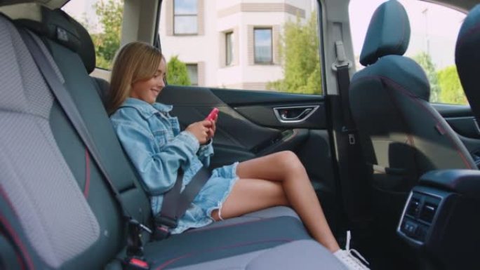 小女孩在后座上用手机的肖像。金发小女孩坐在现代车里玩智能手机