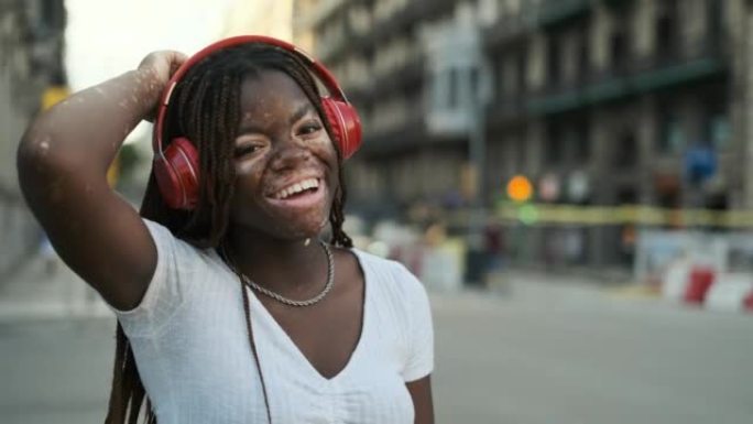白癜风的非洲裔美国妇女在户外的街道上戴着耳机听音乐时微笑着。