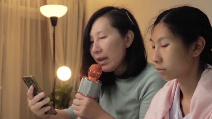 快乐的亚洲妈妈和女儿一起唱一首歌，女儿晚上在家一起坐在沙发上玩电子钢琴，生活理念。