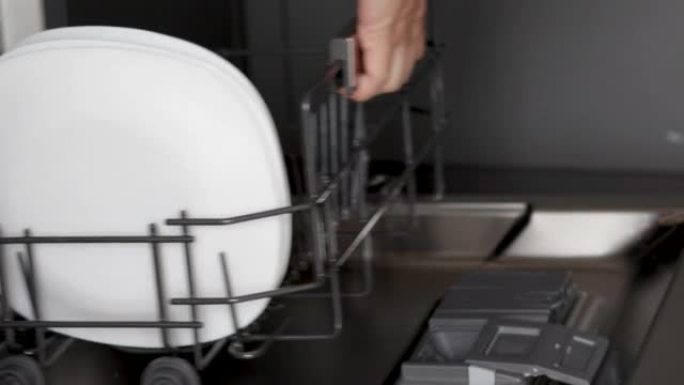 女人从自动洗碗机中取出白色盘子或将洗涤剂荚放入机器中