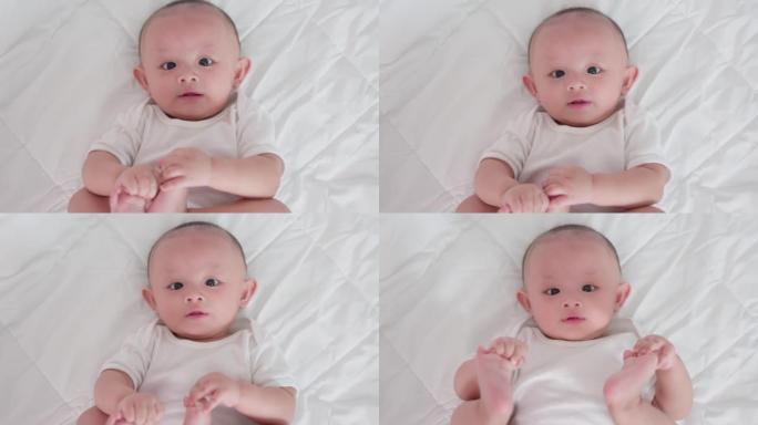 可爱的亚洲新生婴儿躺在白色床上玩耍的肖像看着相机，笑容满面。天真的小新婴儿可爱。父母身份和母亲节概念